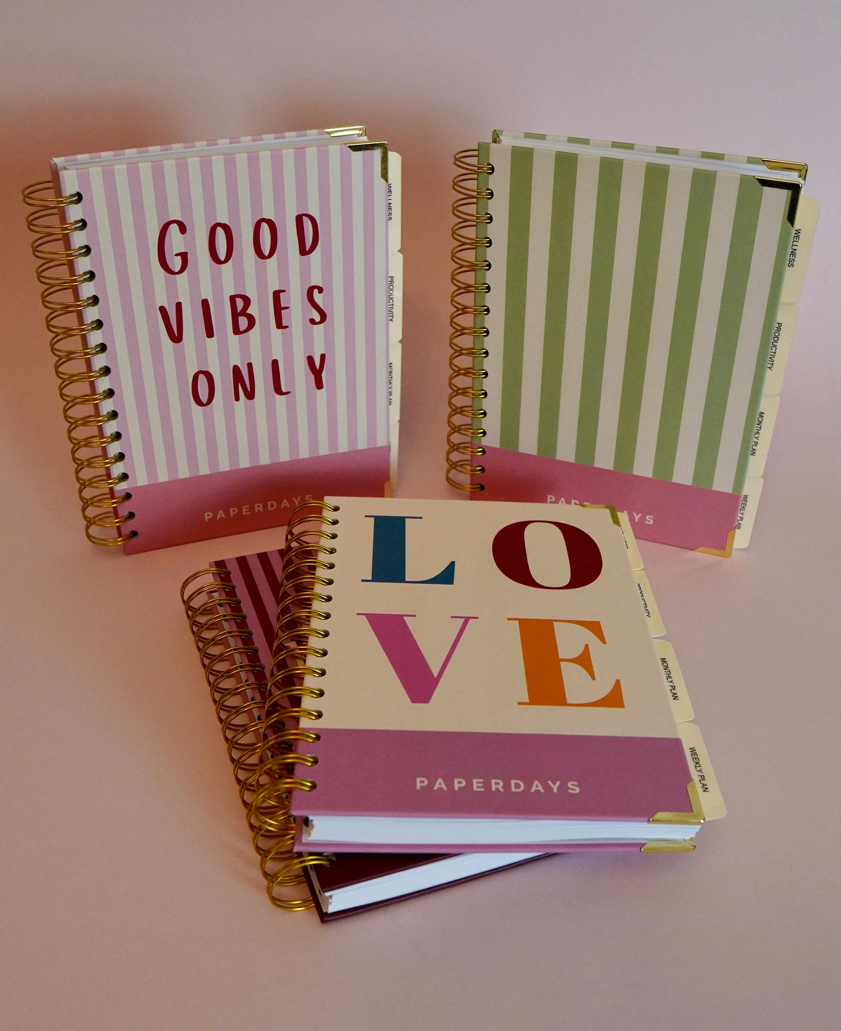Four spiral-bound notebooks with 'Good Vibes Only', 'LOVE', and 'PAPERDAYS' text on a light pink background.
