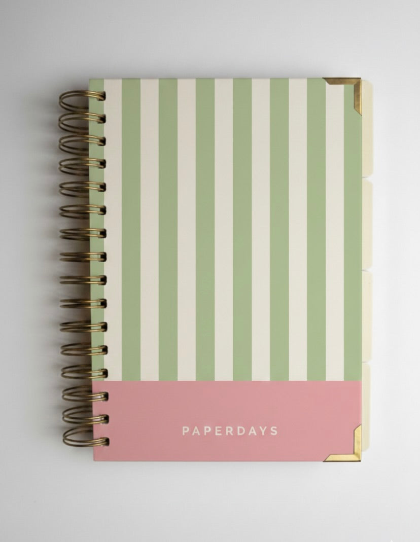 Notebook with green and white striped cover and pink bottom section on a light gray background