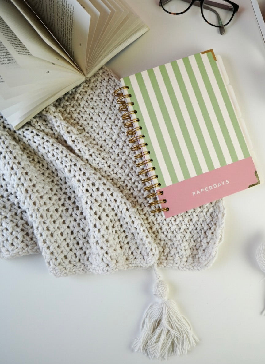 Striped notebook on a textured surface with an open book and glasses in the background