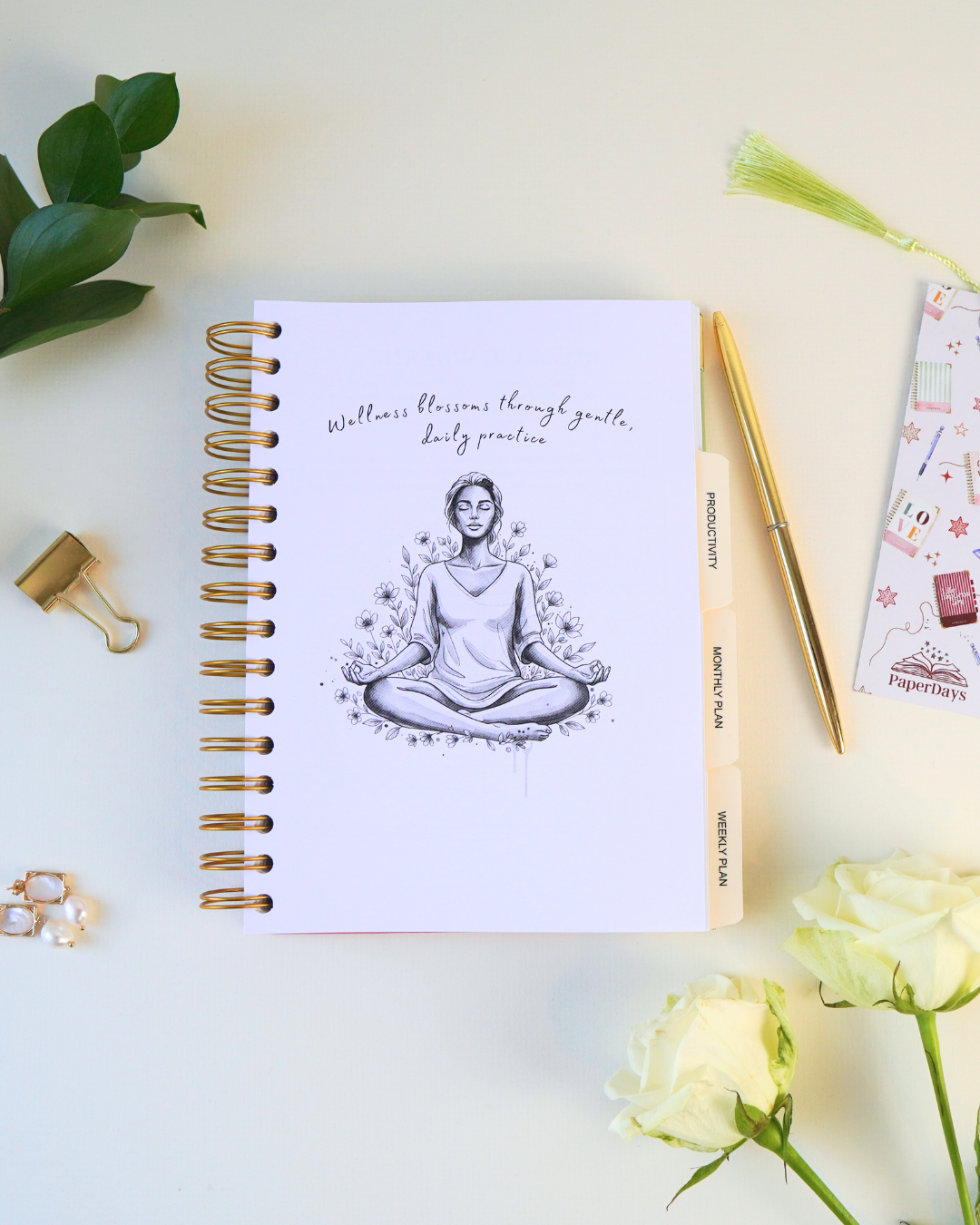 Notebook with a meditation illustration on a white surface with flowers and stationery items.