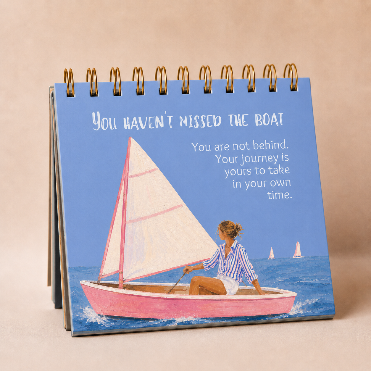 A spiral-bound desk calendar or tabletop print with a blue cover, featuring an illustration of a woman in a pink sailboat on the water and the text, 'YOU HAVEN'T MISSED THE BOAT.'.